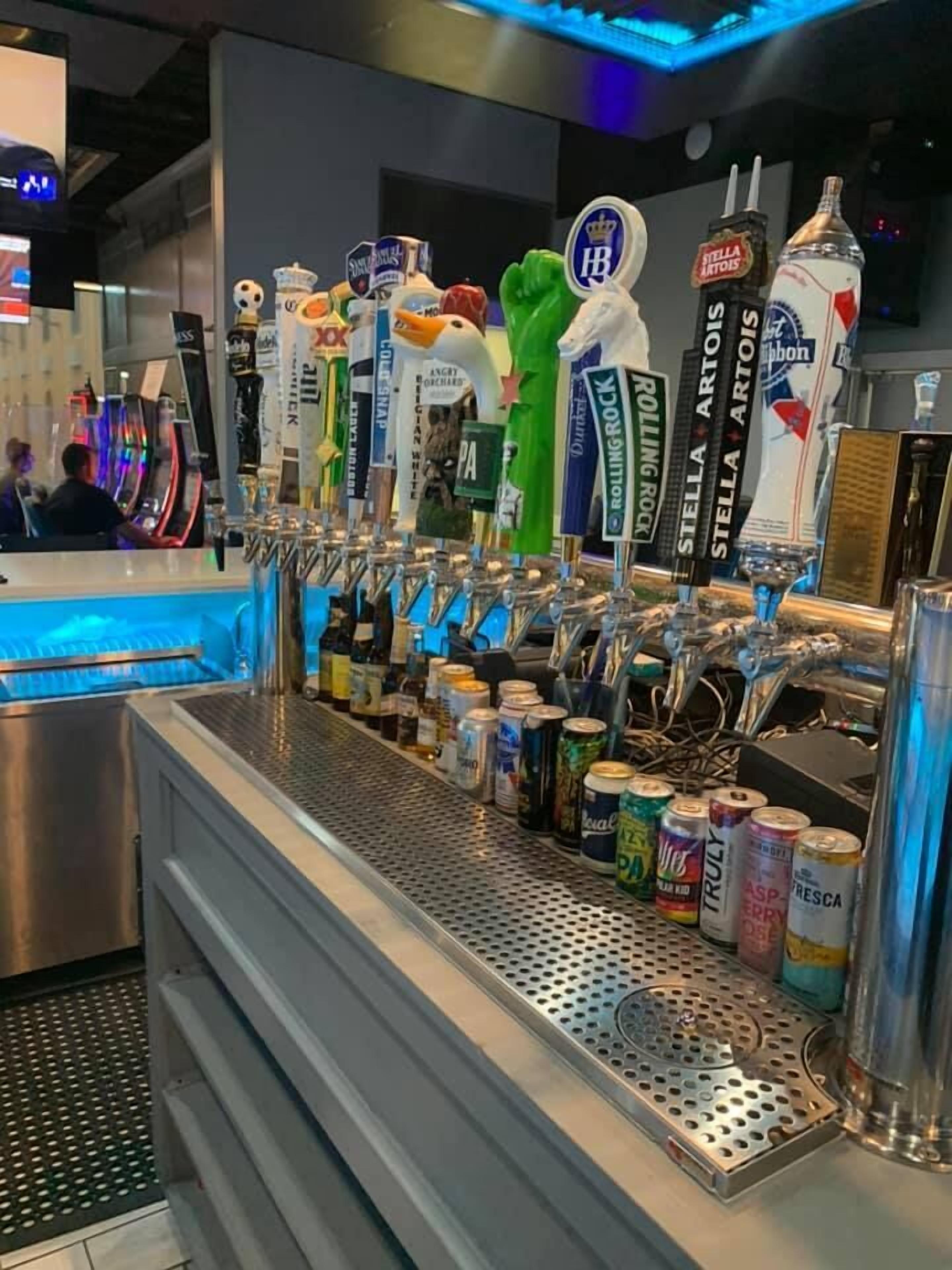 Zona de bar con múltiples grifos de cerveza y una variedad de bebidas en lata.