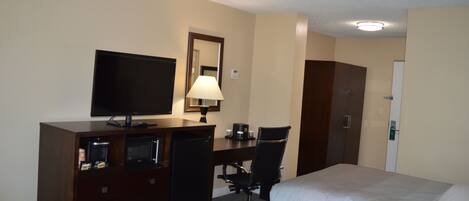 Quarto de hotel com duas camas, uma mesa com computador e luminária, televisão e minibar.