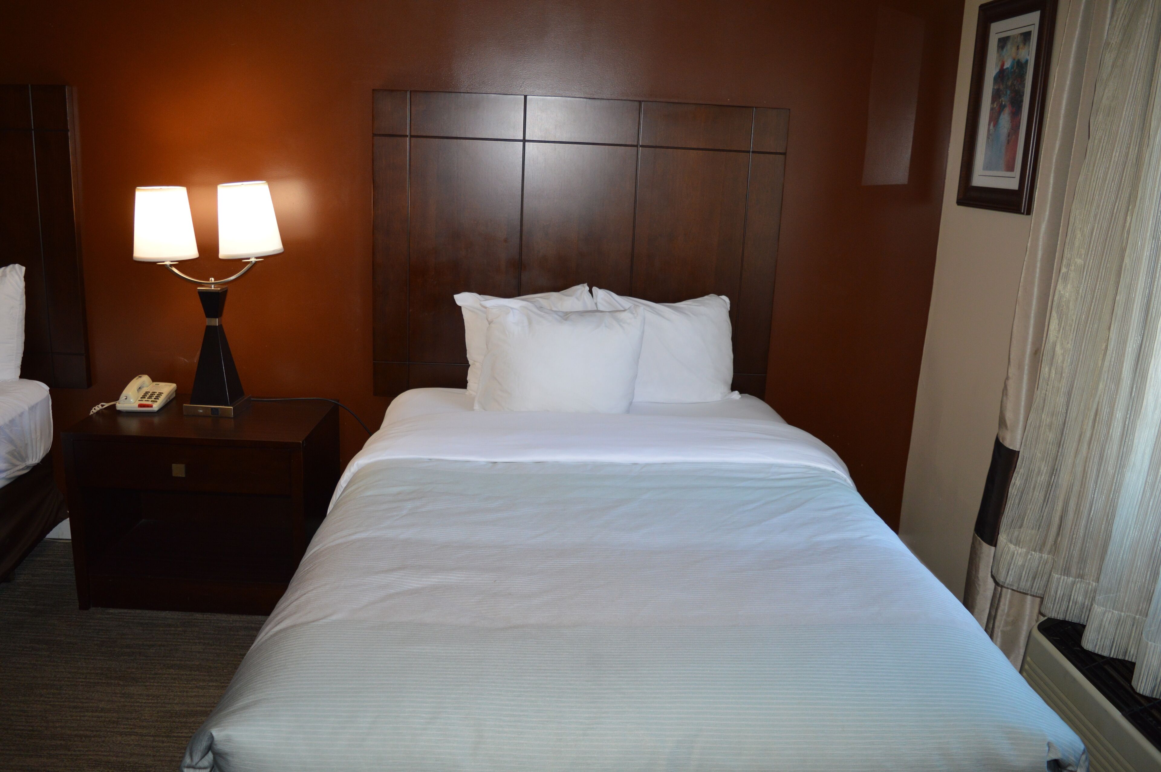 A hotel room with a large bed, a nightstand with a lamp, and a framed picture on the wall.