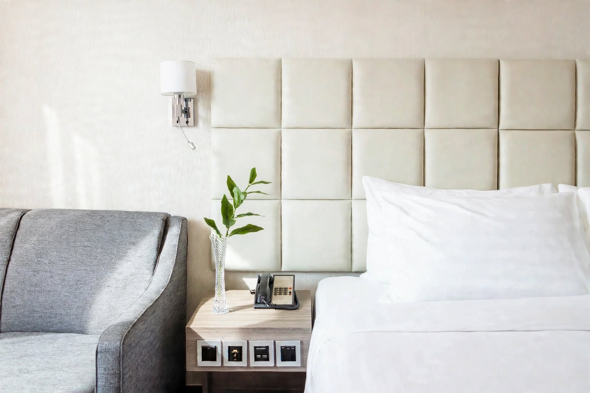 Habitación de hotel con cama, mesita de noche con lámpara, teléfono y planta.