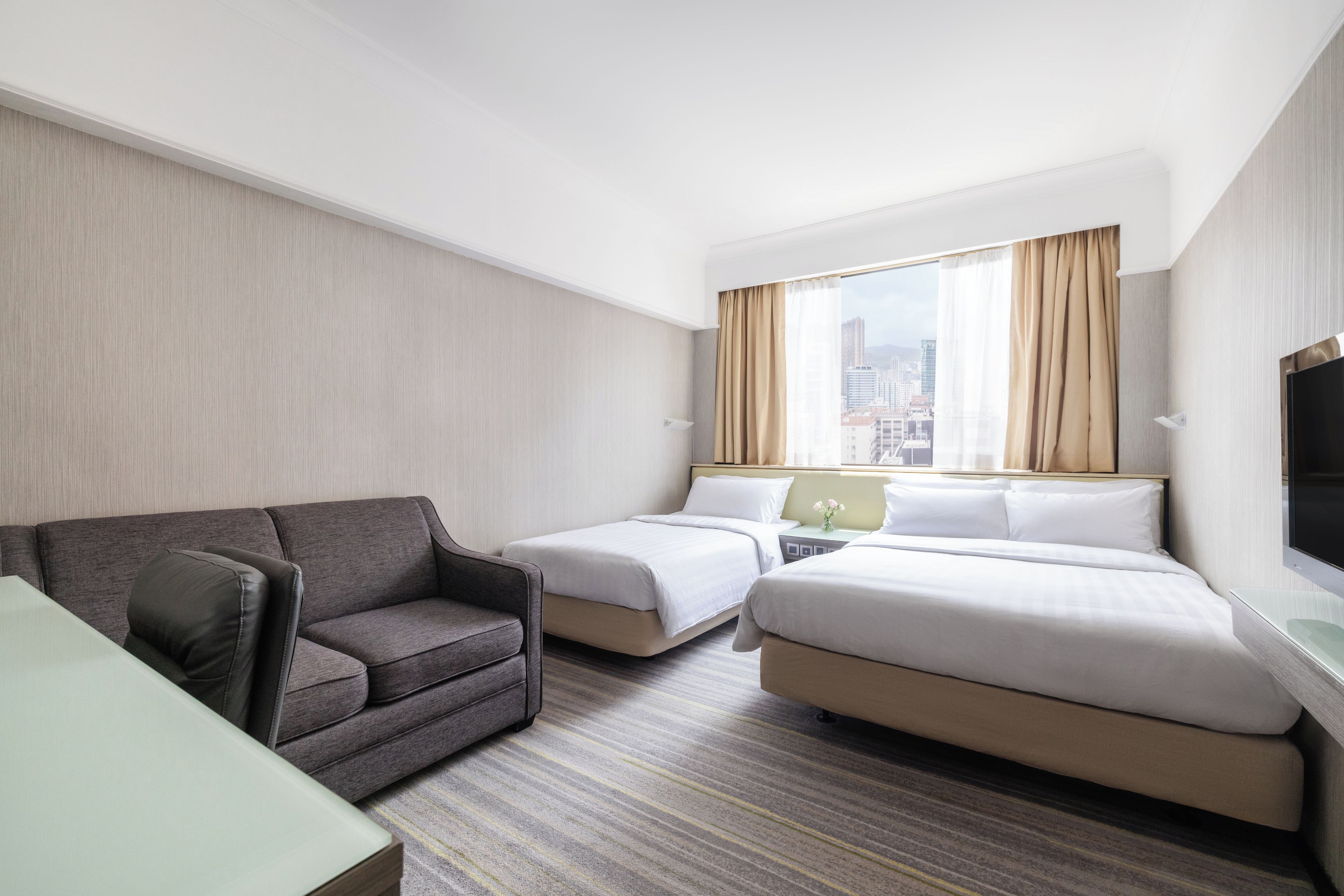 A hotel room with a sofa, two beds, a TV, and a city view.