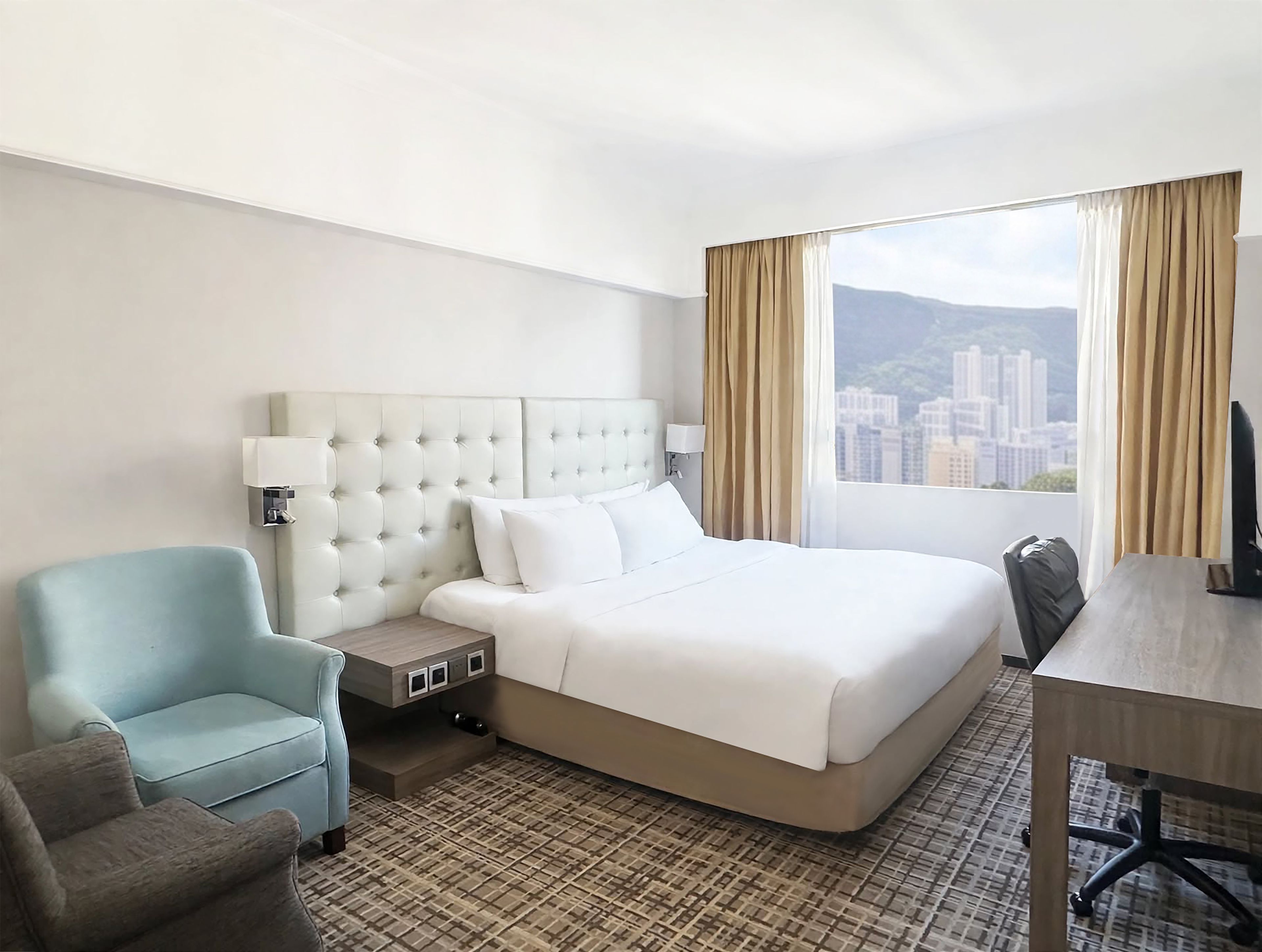 A hotel room with a bed, a desk, a chair, and a view of a cityscape.