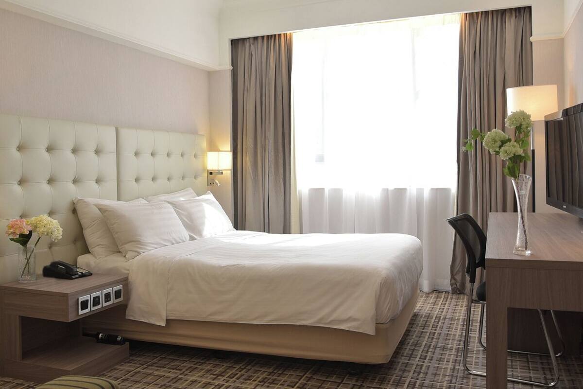 A hotel room with a large bed, bedside tables, a desk, and a chair.
