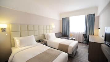A hotel room with two beds, a desk, a chair, a TV, and a window with curtains.