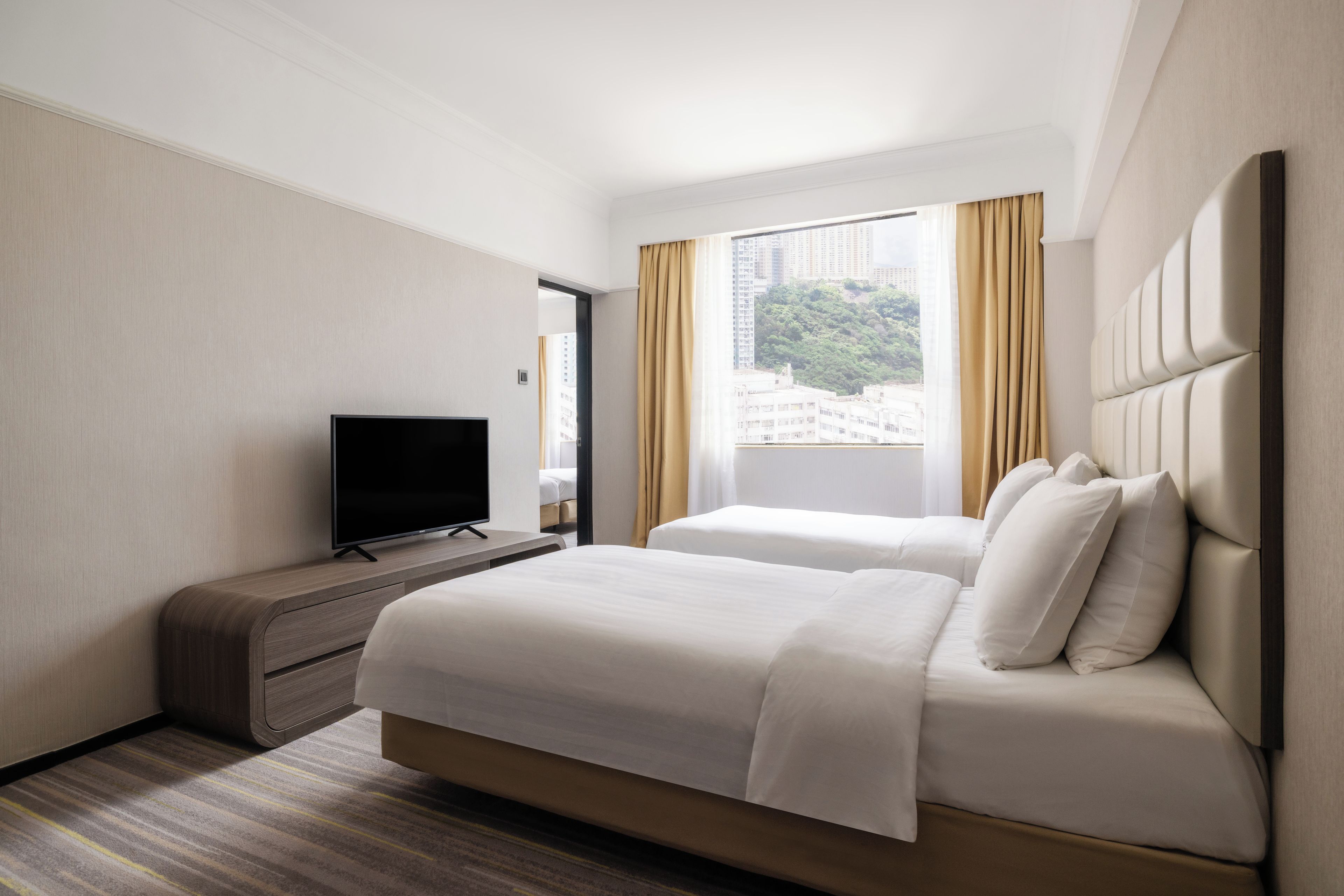 A hotel room with a bed, a television on a stand, and a window with curtains.