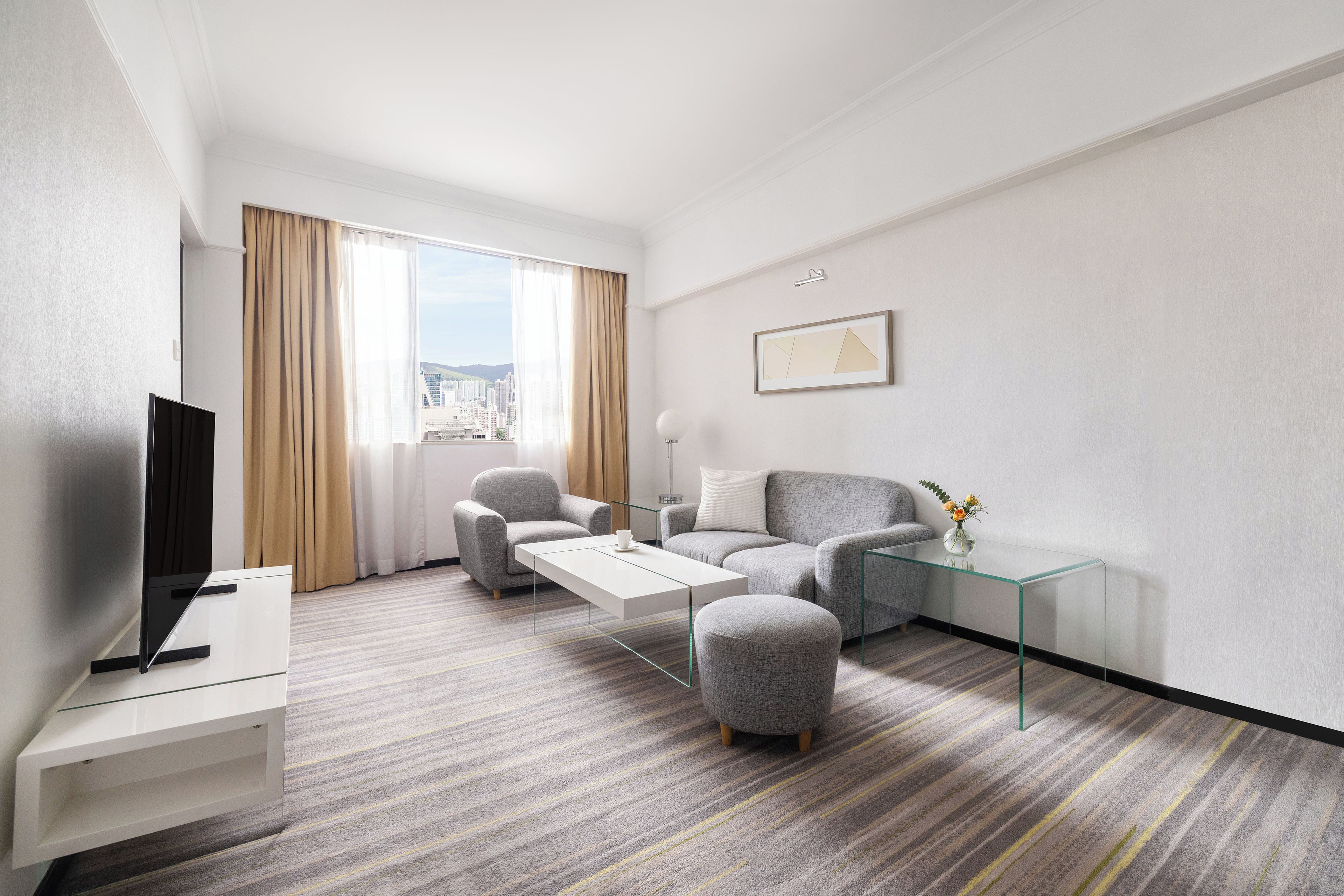 A modern hotel room with a flat-screen TV, a sofa, a coffee table, and a glass side table with a vase.