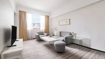 A modern hotel room with a flat-screen TV, a sofa, a coffee table, and a glass side table with a vase.