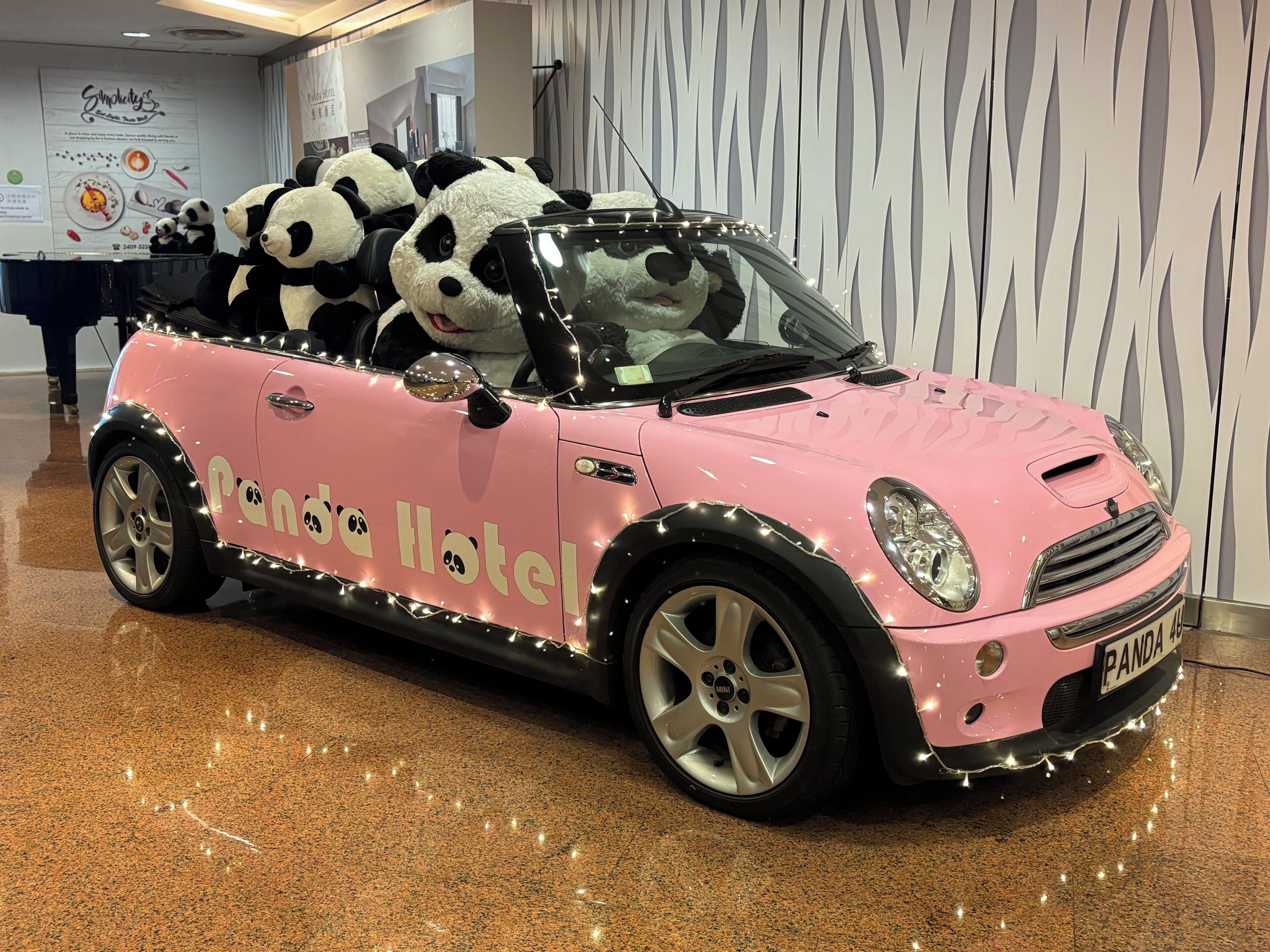 A pink convertible car with 'Panda Hotel' branding and panda plush toys on the roof.