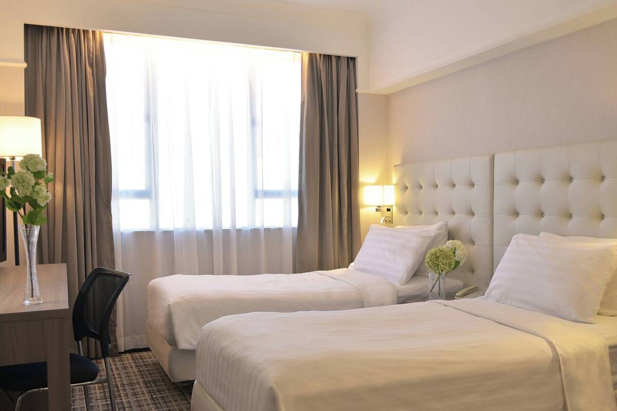 A hotel room with two beds, a desk, a chair, and a large window with curtains.