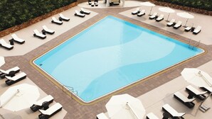 A rectangular swimming pool surrounded by lounge chairs and umbrellas, with a brick border and a covered seating area in the background. - Panda Hotel (Tsuen Wan)
