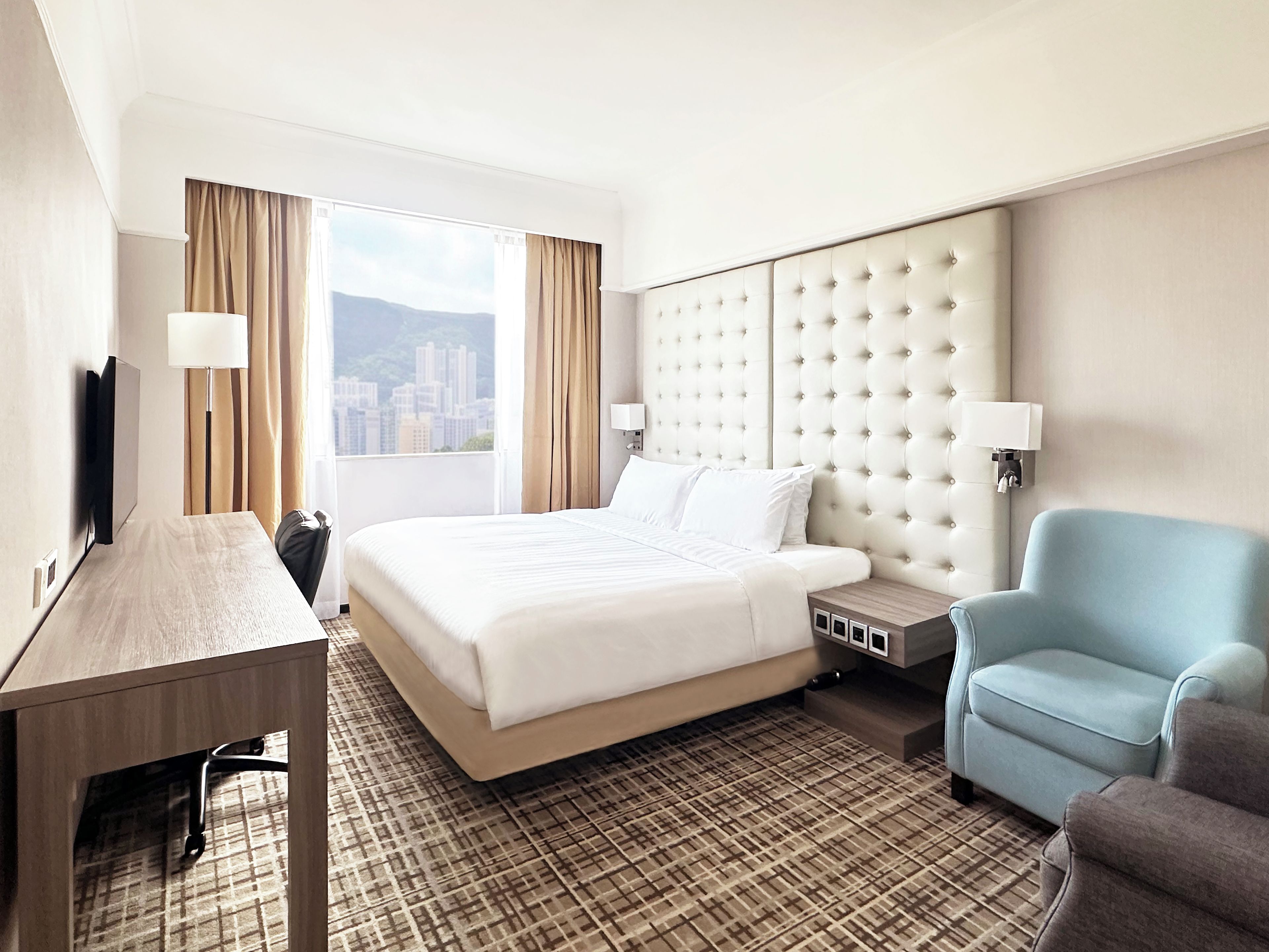A hotel room with a large bed, a desk, a chair, and a view of the city.