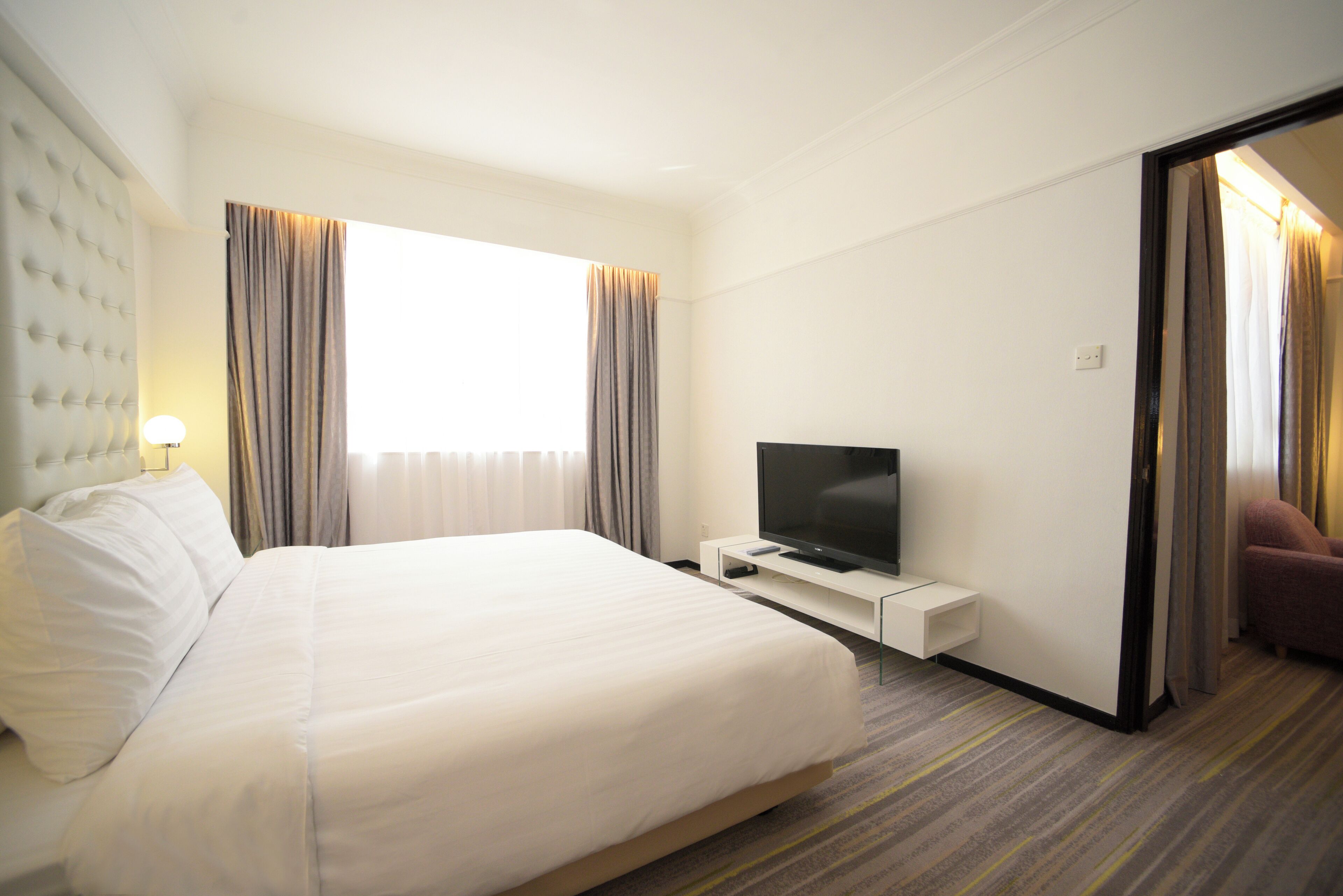 Habitación de hotel con una cama grande, televisor de pantalla plana, mesita de noche y ventana con cortinas.