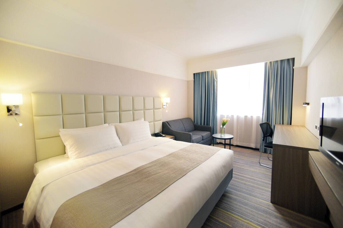 A hotel room with a large bed, a desk, a chair, a TV, and a window with curtains.