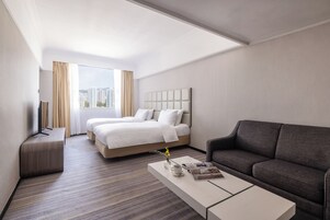 Quarto de hotel com duas camas, um sofá, uma mesa de centro e uma televisão.