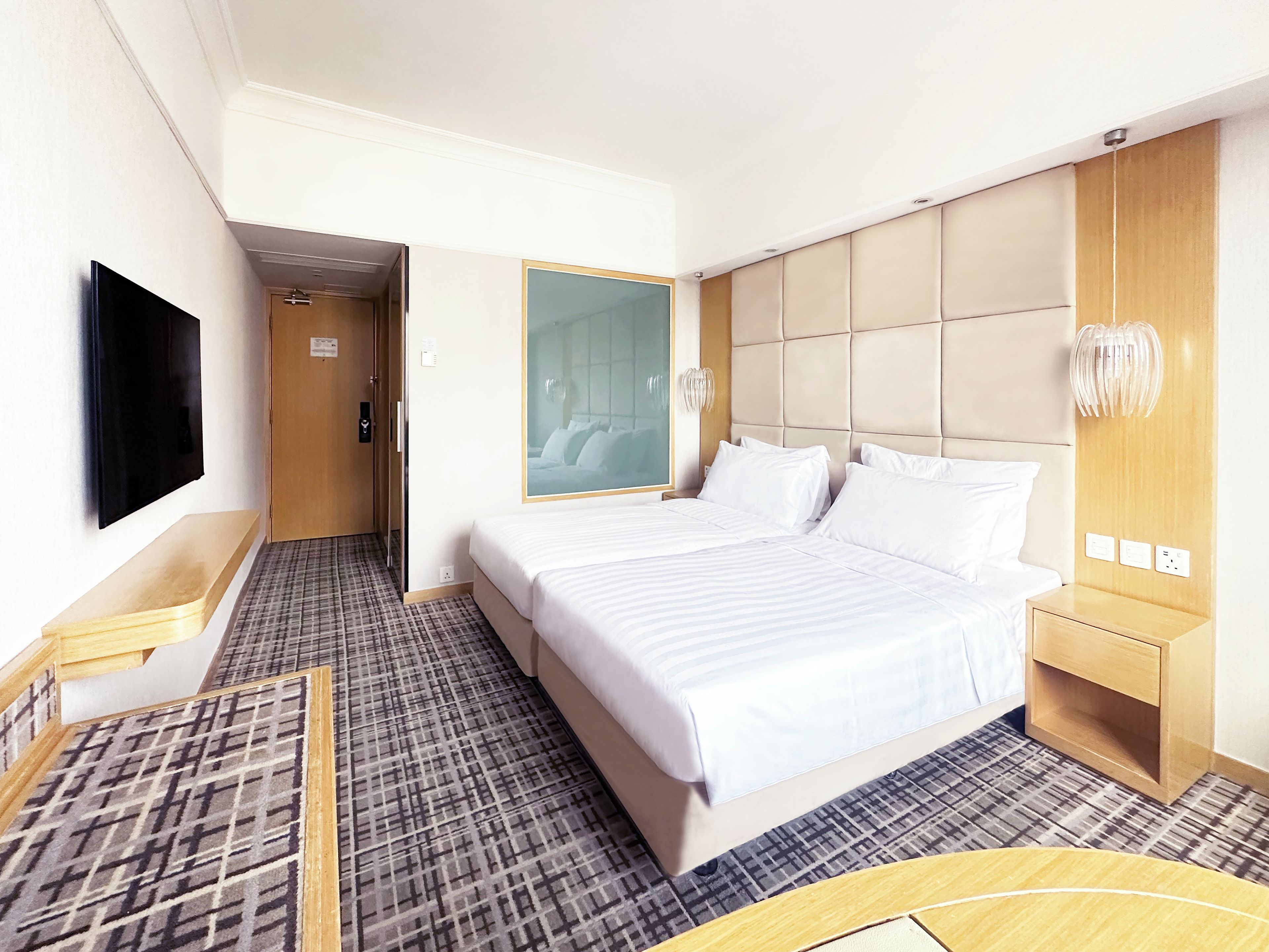 Ein Hotelzimmer mit einem großen Bett, einem Fernseher, einem Spiegel und einem Nachttisch aus Holz.