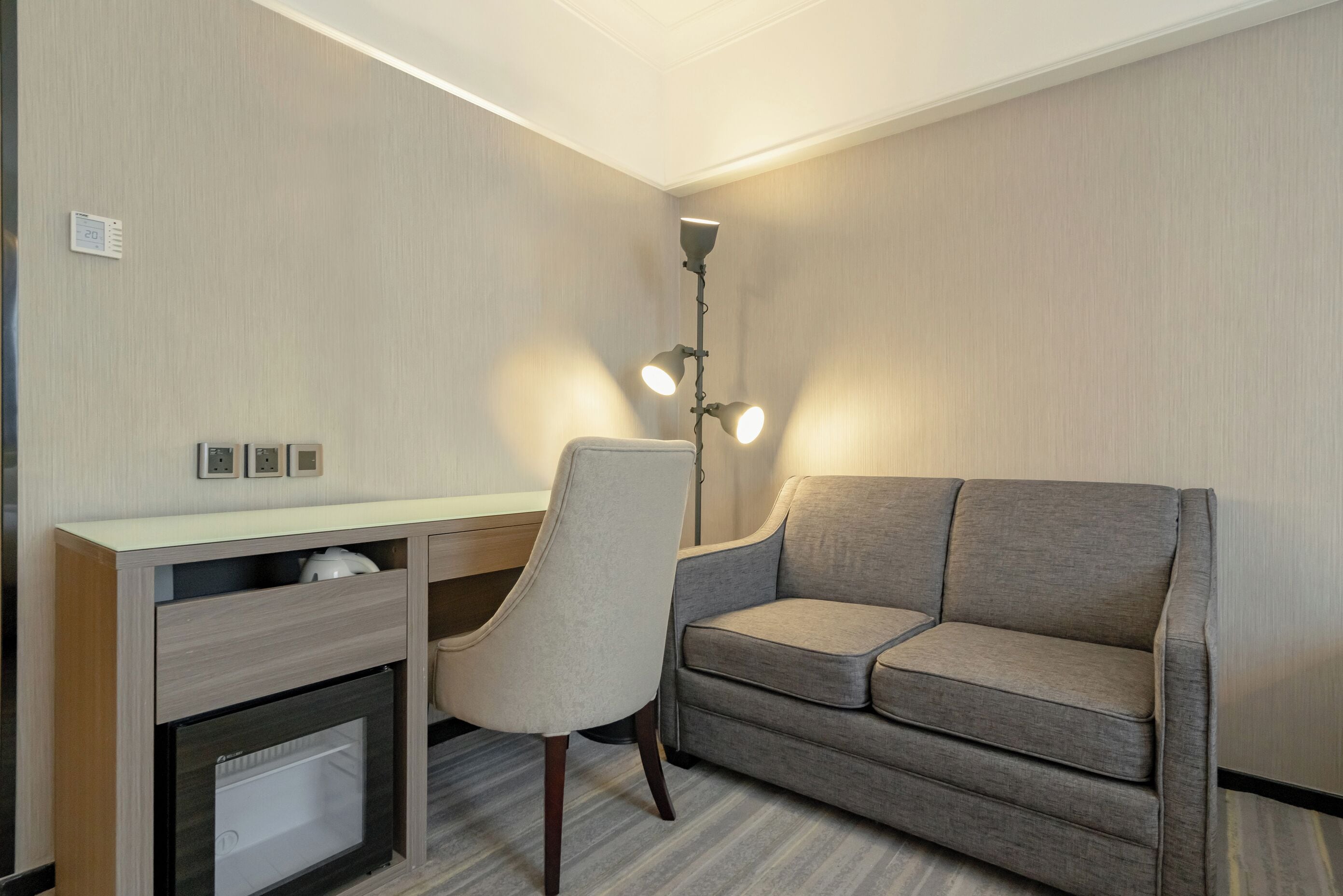 A hotel room with a desk, chair, sofa, and a floor lamp.
