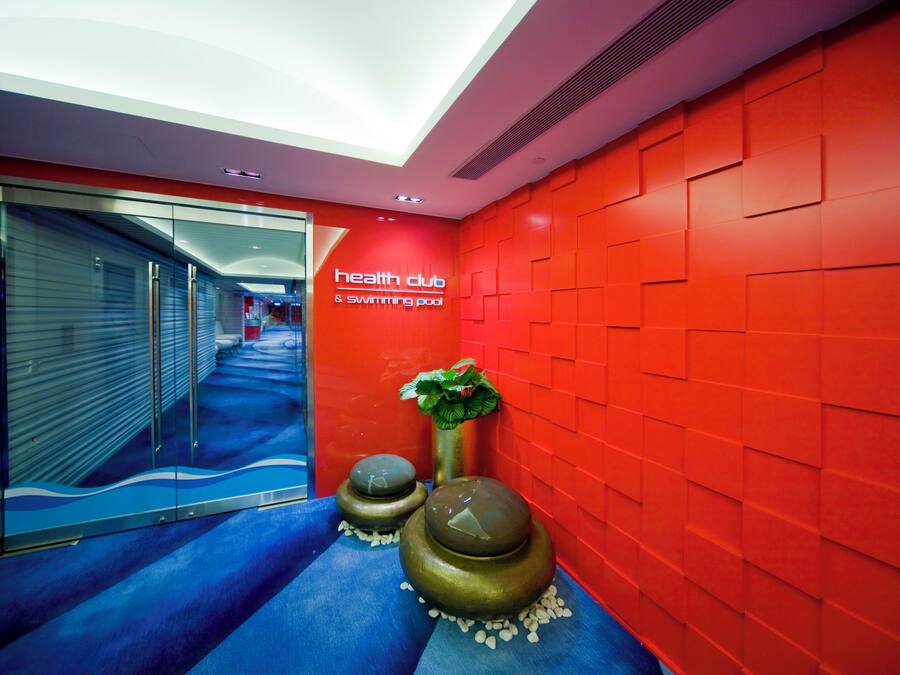 Um corredor com parede vermelha, uma placa indicando "health club & swimming pool" e duas esferas no chão.