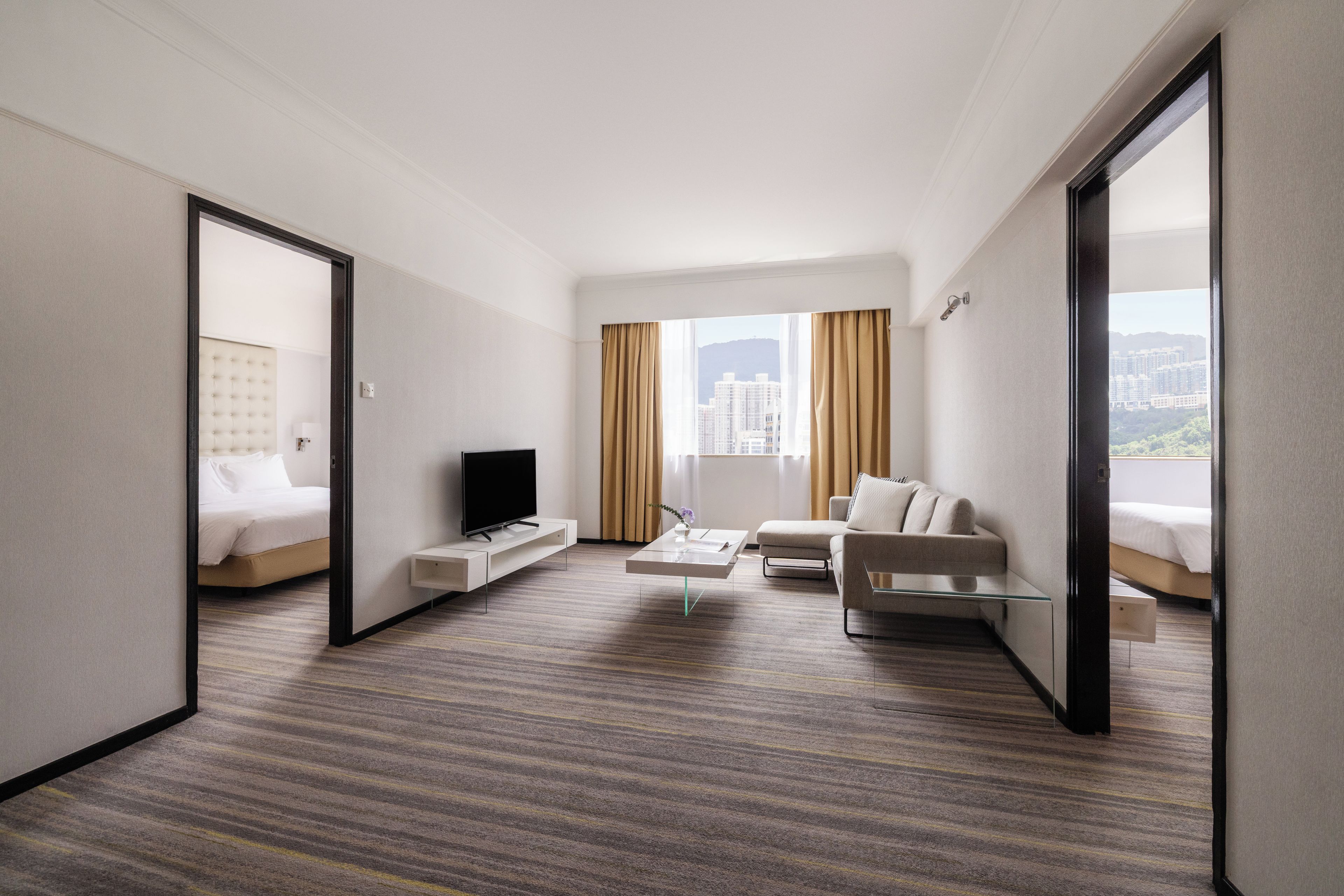 A hotel room with a bed, a TV, a sofa, and a view of the city.
