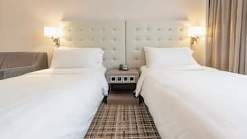 A hotel room with two beds, a headboard with a mirror, bedside lamps, a nightstand, and a patterned carpet.