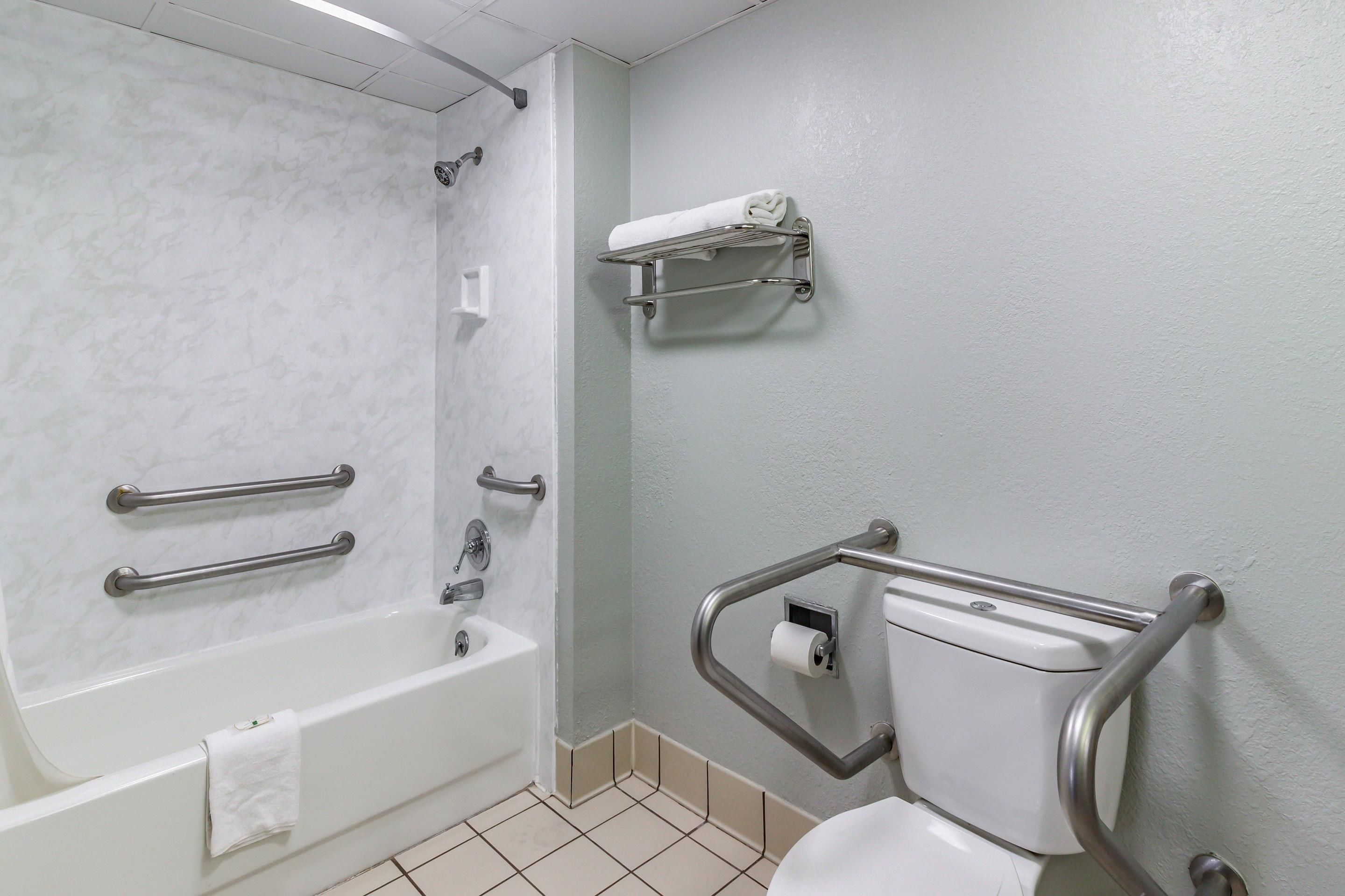 A bathroom with a bathtub, toilet, and handrails.