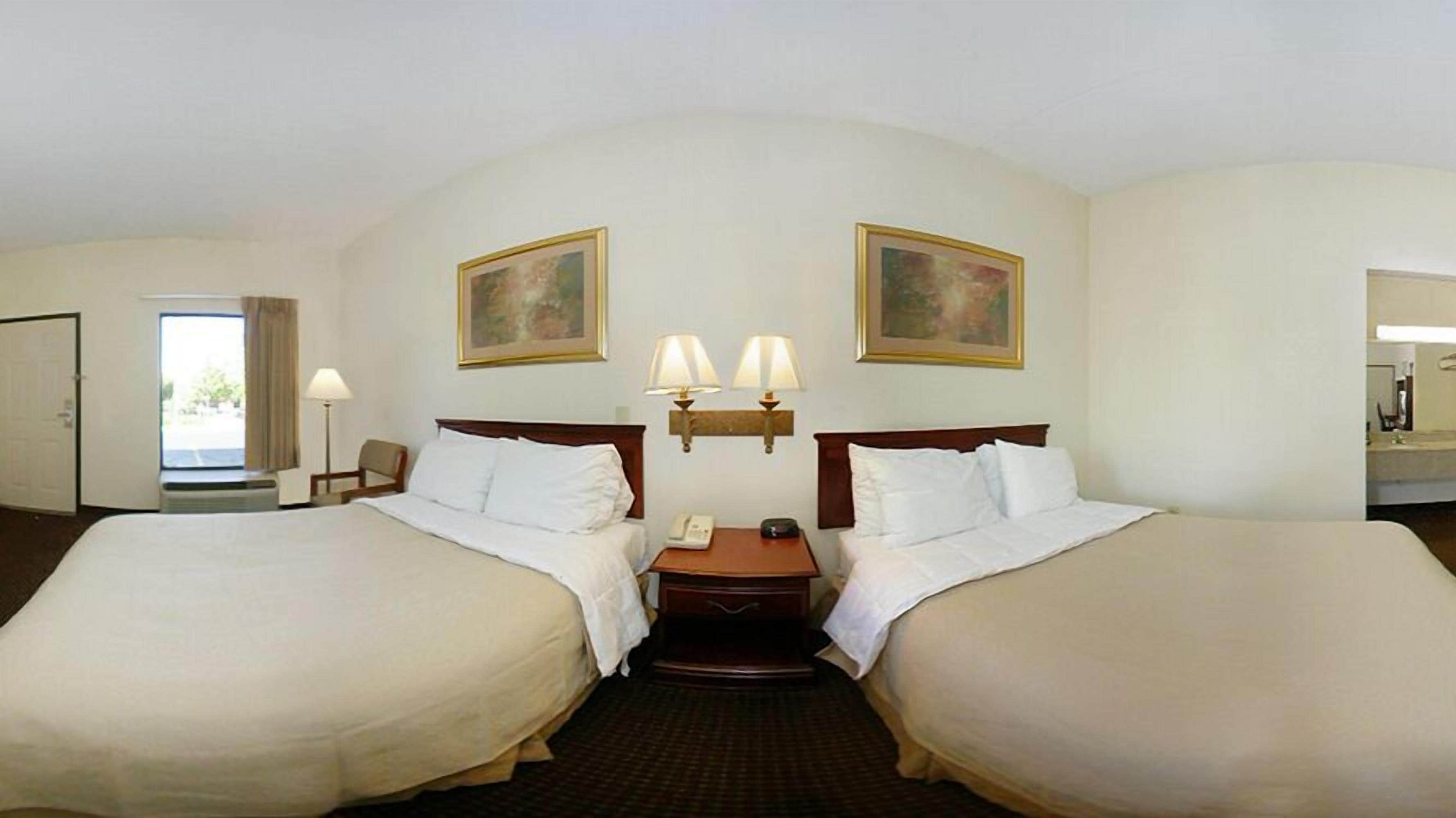 A hotel room with two beds, a bedside table with a lamp, a phone, and a clock.