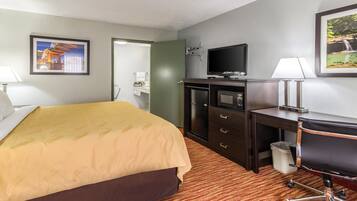 A hotel room with a bed, a desk, a television, and a trash can.