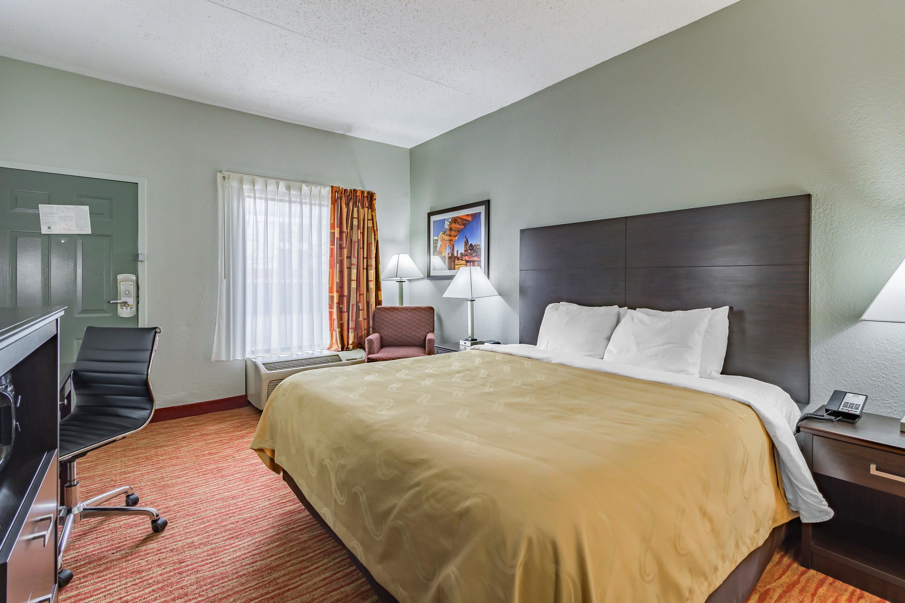 A hotel room with a large bed, a desk with a chair, a lamp, and a painting on the wall.