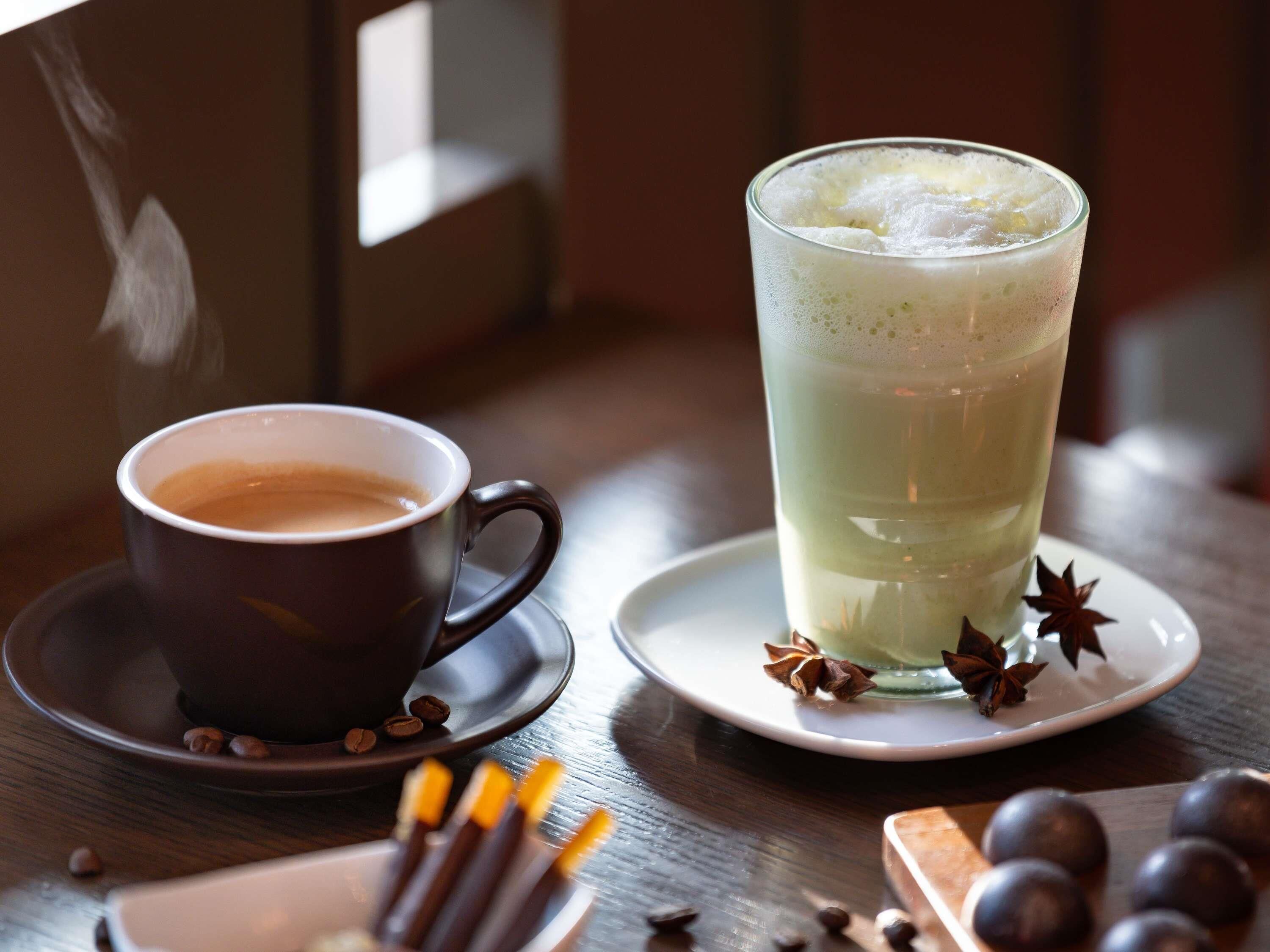 Una taza de café y un vaso de té verde sobre una mesa de madera, con anís estrellado y granos de café.
