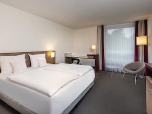 A hotel room with a large bed, a desk, a chair, and a window with curtains. - Mövenpick Hotel Münster am Aasee (Münster)