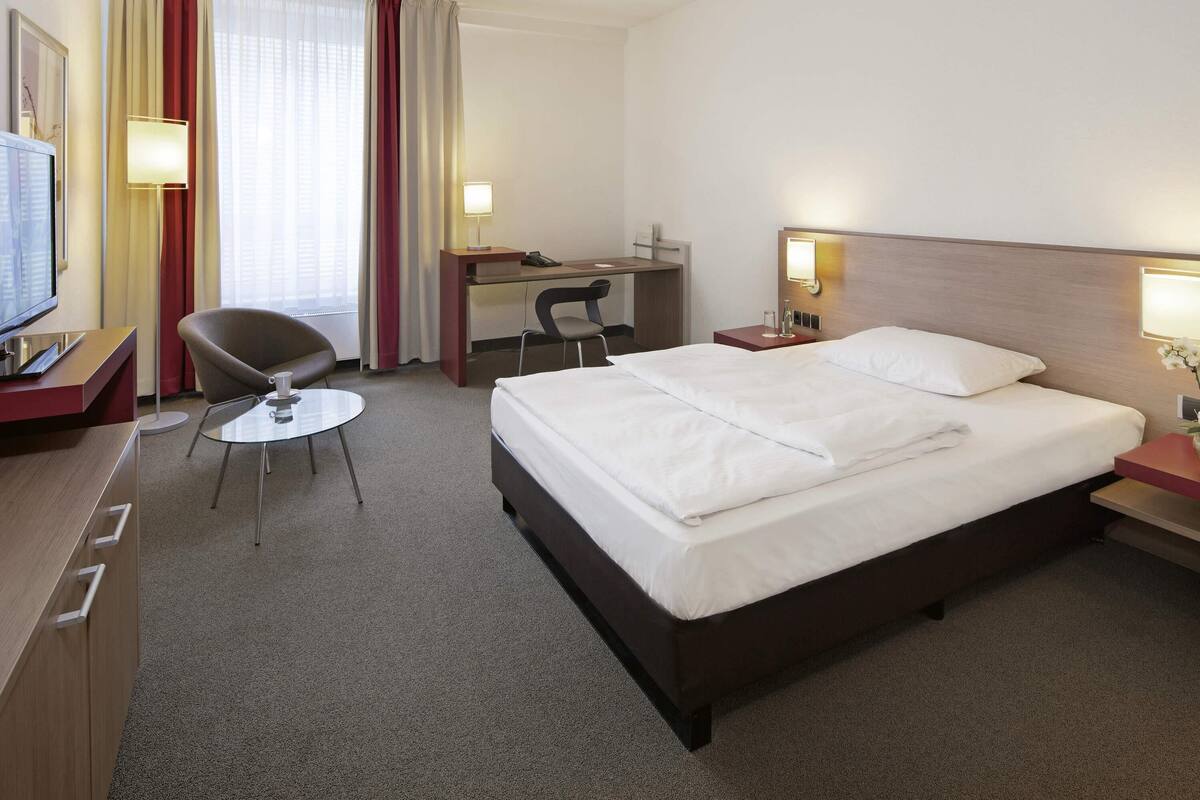 A hotel room with a bed, desk, chair, and a television.