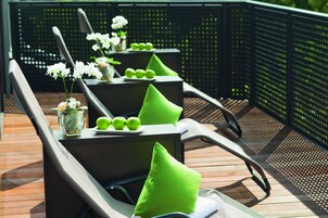A deck with lounge chairs, each with a green cushion and a small potted plant.