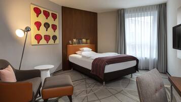 Une chambre d’hôtel avec un lit, un bureau, une chaise, une lampe et un tableau au mur.