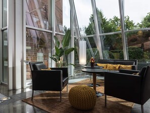 Un intérieur moderne avec un mur de verre, des canapés noirs, un pouf jaune rond et une table sur laquelle est posé un vase de fleurs.