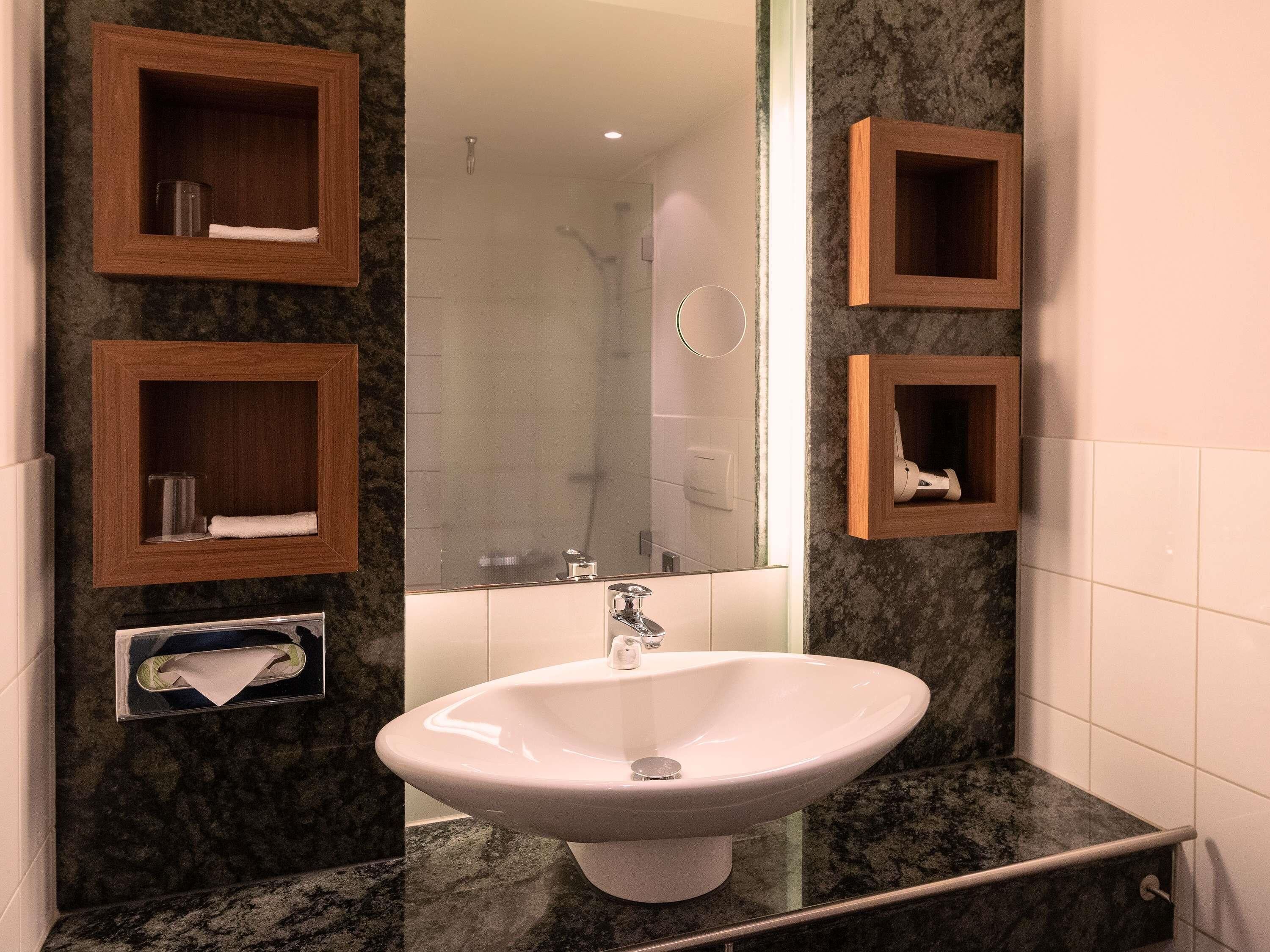 A bathroom with a white sink, wooden medicine cabinets, a mirror, and a shower area.