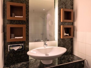 A bathroom with a white sink, wooden medicine cabinets, a mirror, and a shower area. - Mövenpick Hotel Münster am Aasee (Münster)