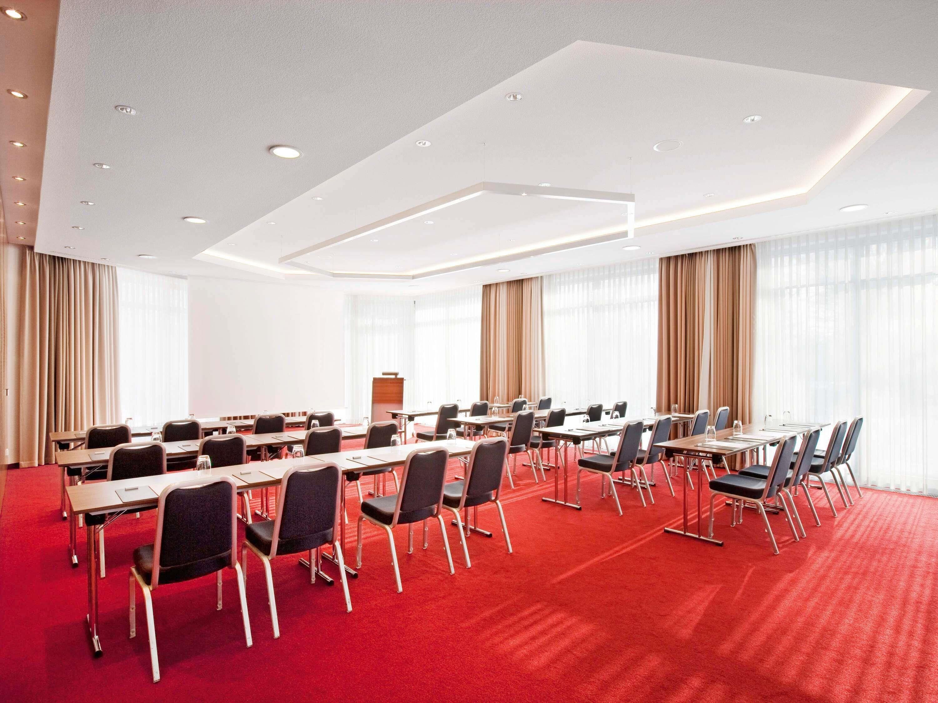 A conference room with a red carpet, multiple tables, chairs, and a podium.