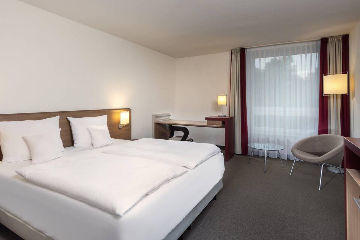 A hotel room with a large bed, a desk, a chair, and a window with curtains.