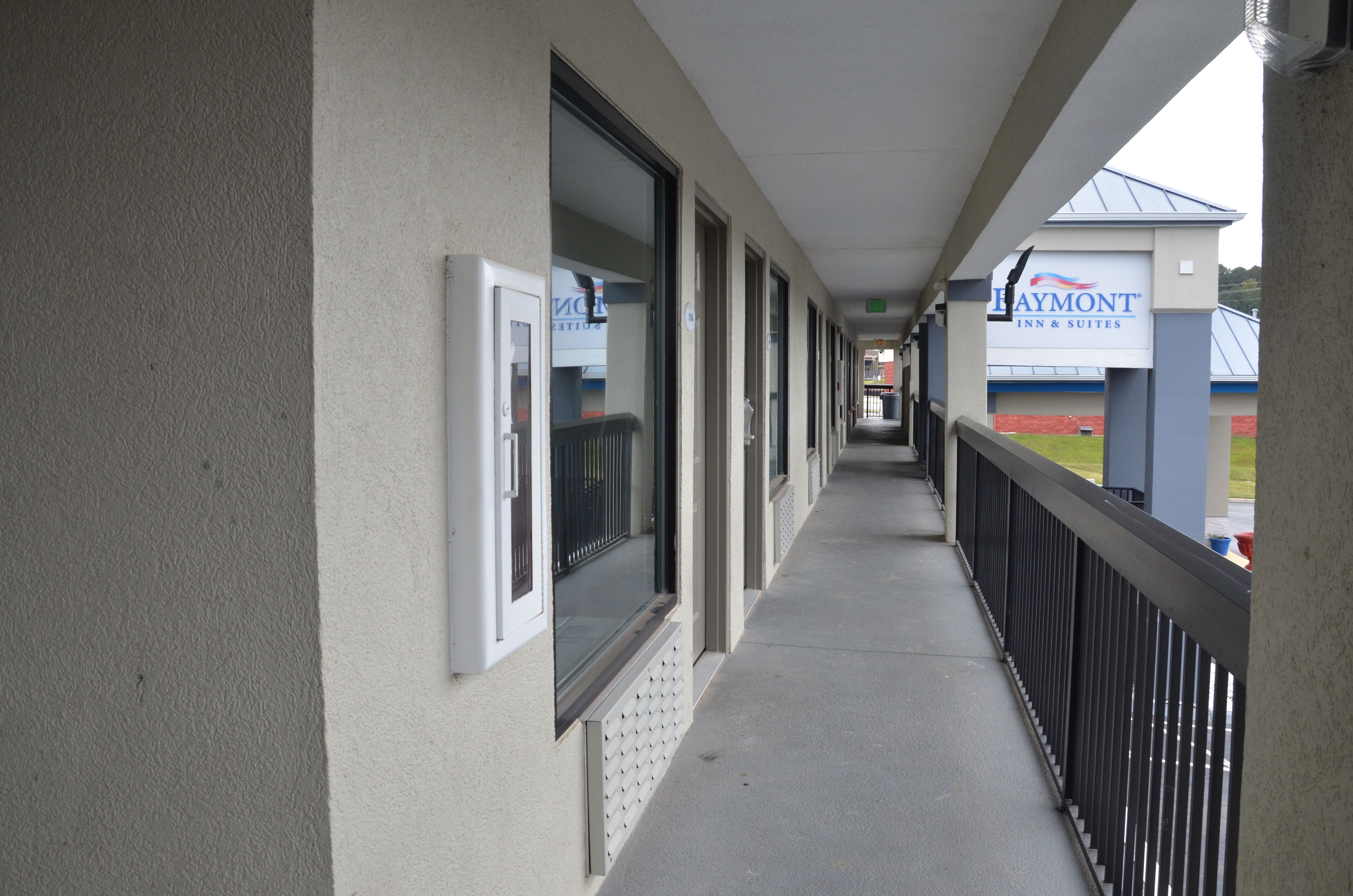 A hotel corridor with a covered walkway, a sign for 'Haymont Inn & Suites', and a view of a baseball field in the background.
