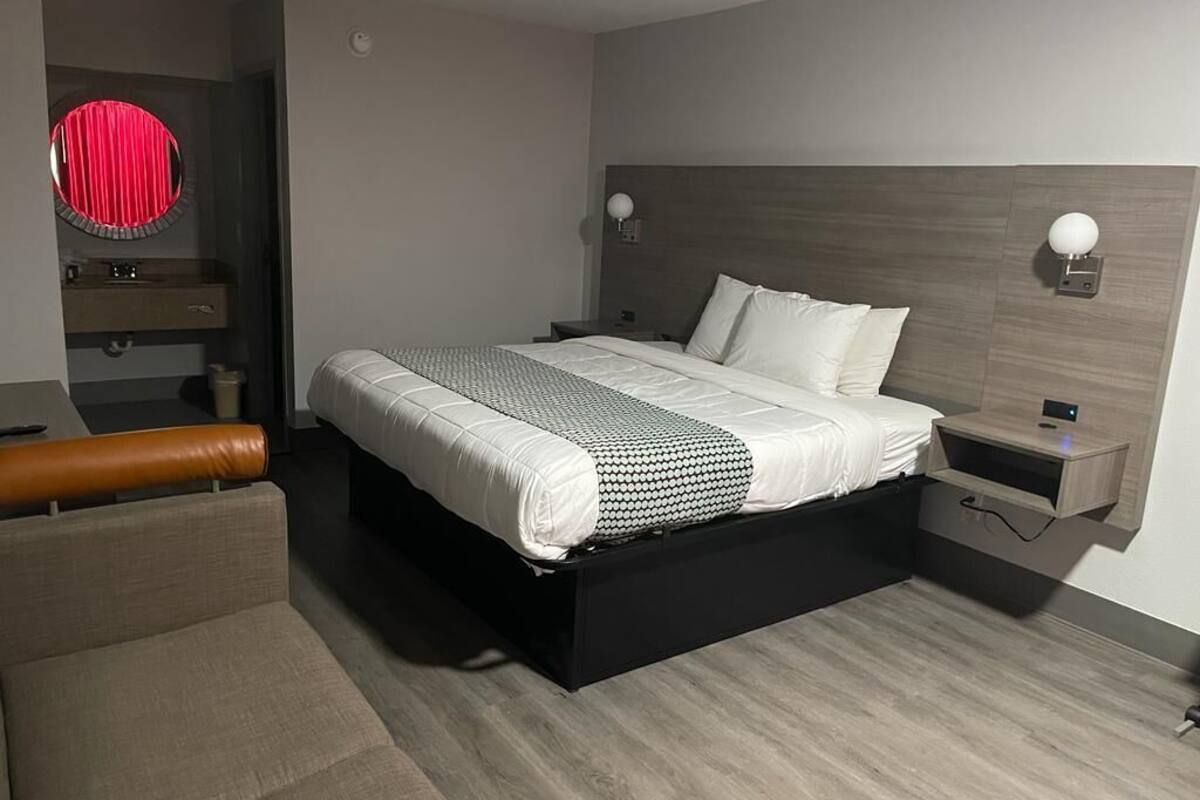 Quarto moderno com cama, mesas de cabeceira, um banquinho e um espelho.