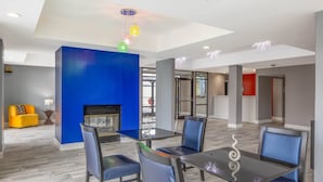 A modern dining area with a blue accent wall, a fireplace, and a glass table with chairs. - Baymont by Wyndham Covington (Covington)