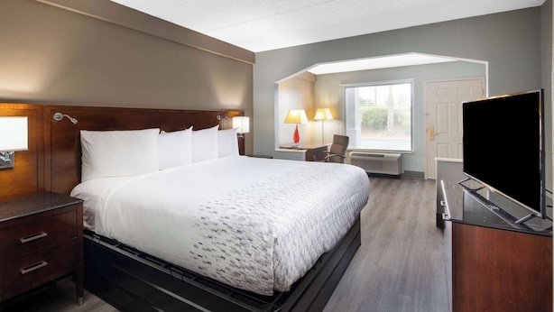 A hotel room with a large bed, bedside tables, a desk with a chair, a flat-screen TV, and a window with blinds. - Baymont by Wyndham Covington (Covington)