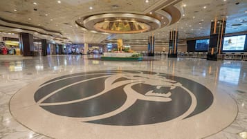 Un hall d’entrée spacieux, orné d’un grand emblème circulaire sur le sol, d’un luminaire décoratif central et d’un écran numérique diffusant du contenu.