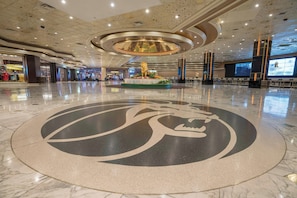 Un hall d’entrée spacieux, orné d’un grand emblème circulaire sur le sol, d’un luminaire décoratif central et d’un écran numérique diffusant du contenu.