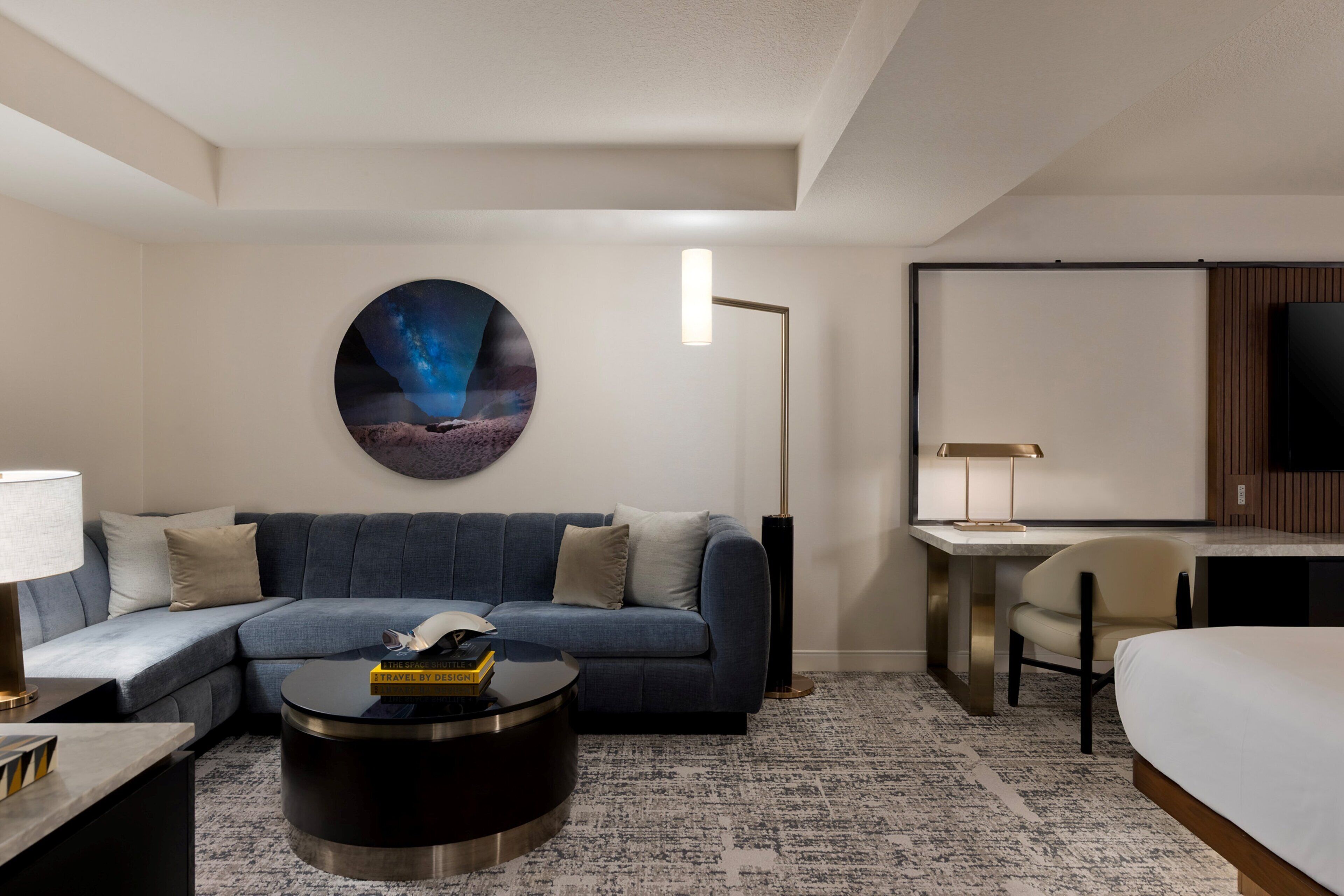 Une chambre d’hôtel moderne comprenant un canapé d’angle, une table basse ronde, un bureau et un lit.