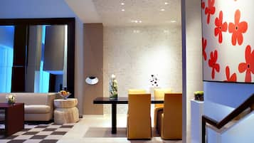 A modern interior with a checkered floor, a dining area with yellow chairs, and a wall with a floral pattern.