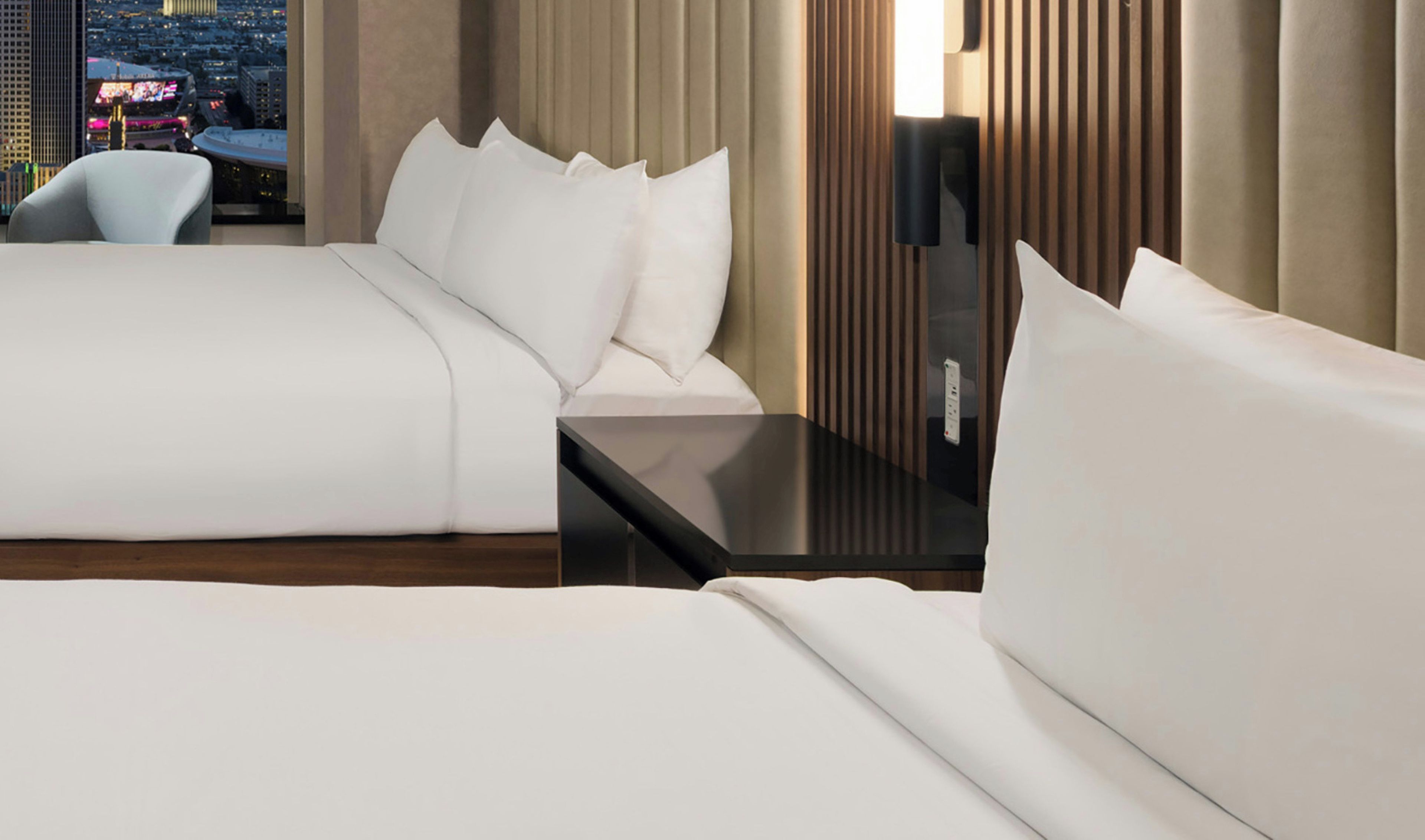 A hotel room with a bed, a bedside table, a chair, and a view of a cityscape.