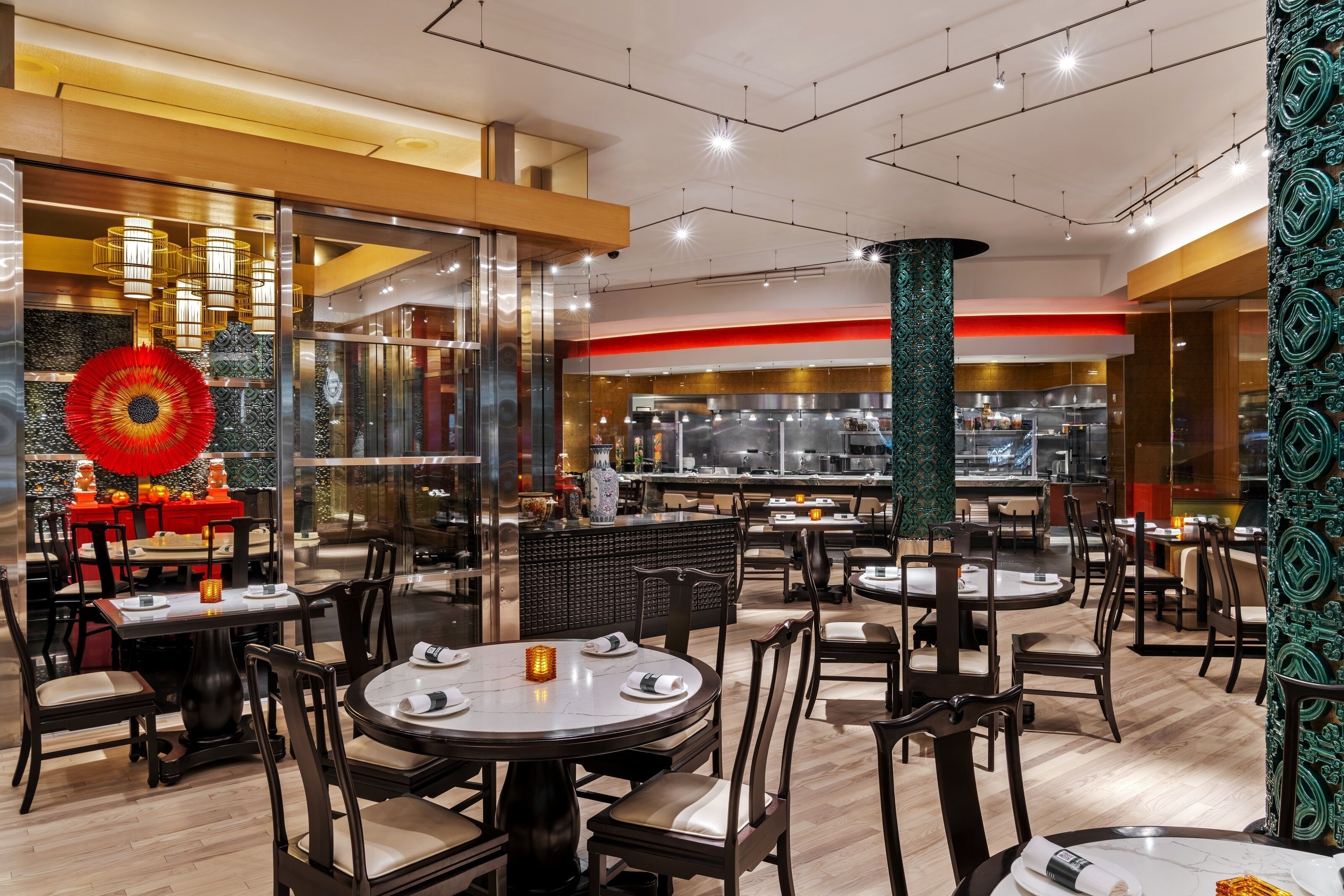 En moderne restaurant med runde borde og stole, et synligt køkkenområde og en dekorativ rød ventilator.