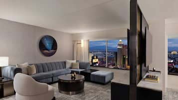 A modern living room with a large sofa, a round coffee table, and a television. The room features a large window with a city view.