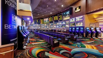 A casino with multiple betting machines, a colorful carpet, and a large screen displaying sports events.