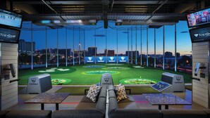 A golf simulation room with a city view, multiple screens, and a seating area with a golf cart. - MGM Grand Hotel & Casino (Las Vegas)
